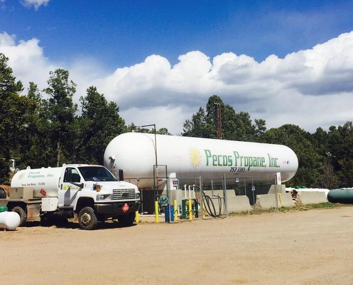 White propane tank and tanker truck at Pecos Propane Inc. on a sunny day.