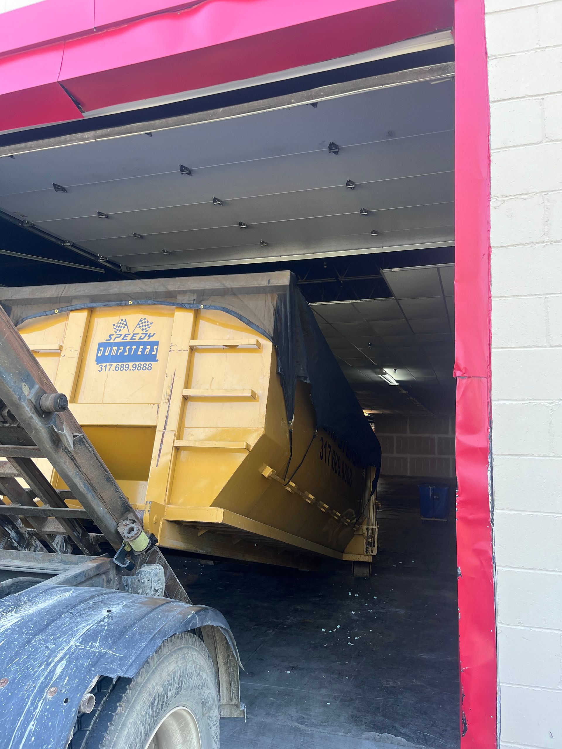 Yellow dumpster being loaded at a red and white loading dock.