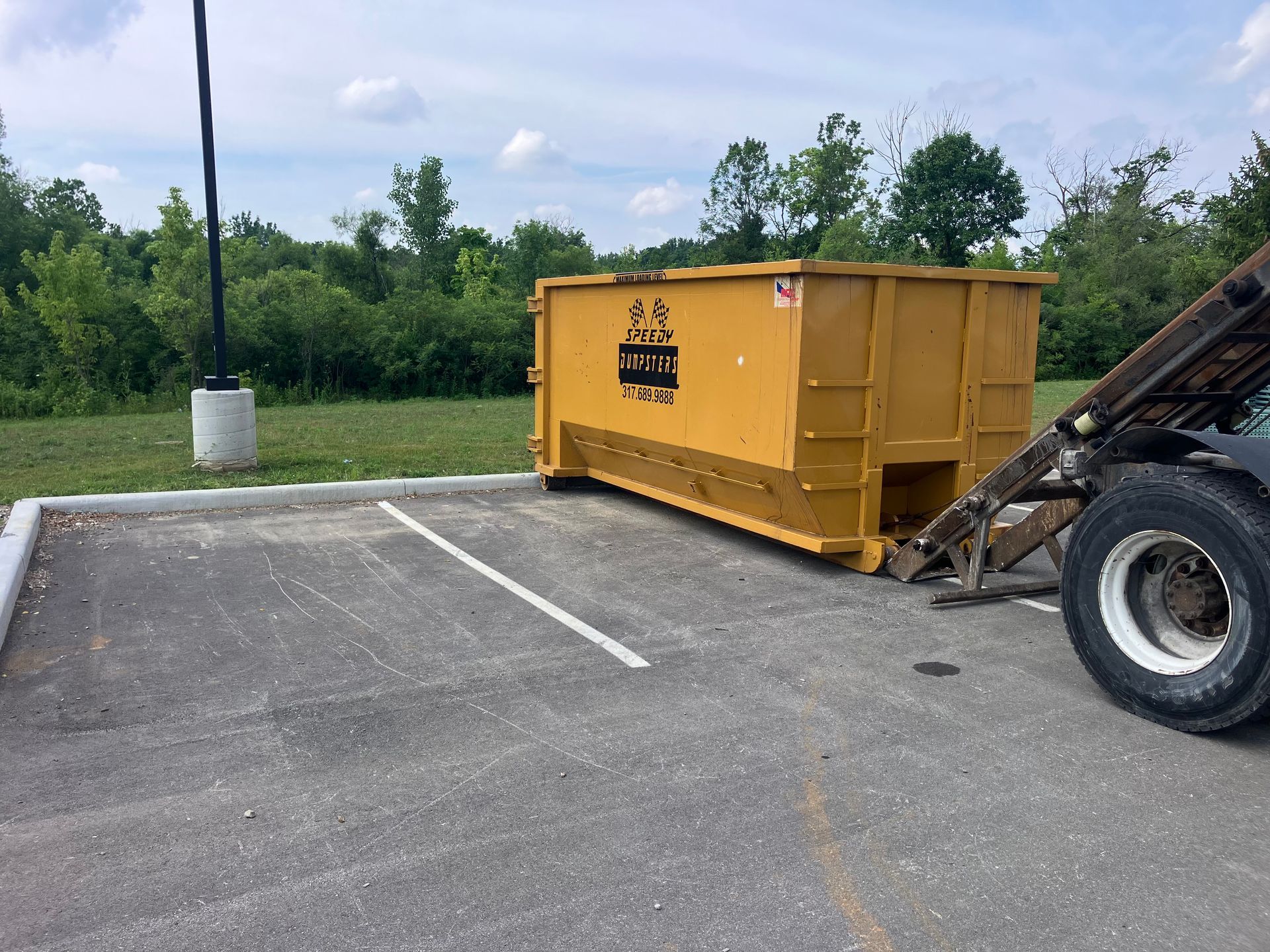 Yellow dumpster in parking spot being serviced by a truck.