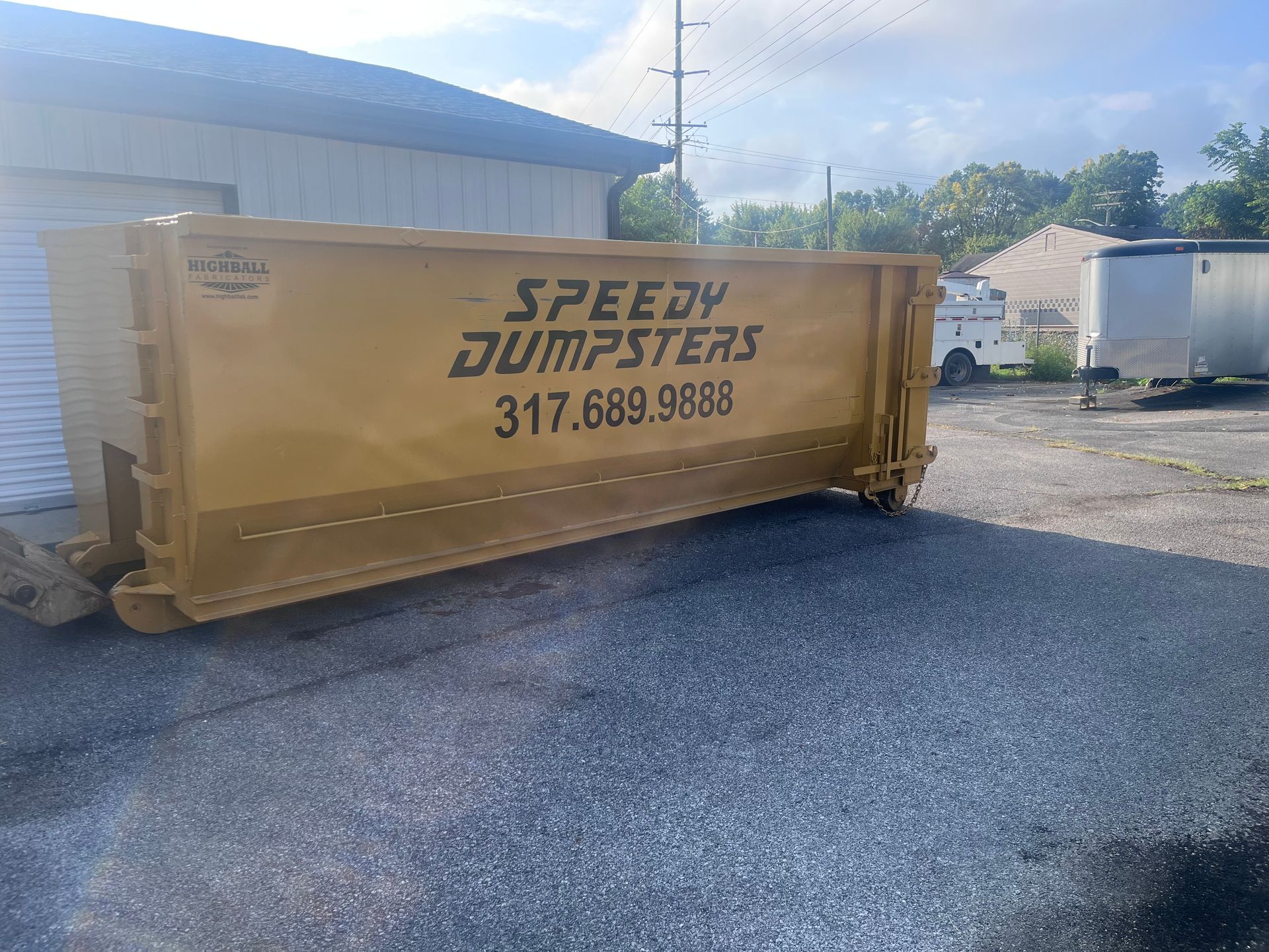 Yellow Speedy Dumpsters dumpster on asphalt; building and sky in background.