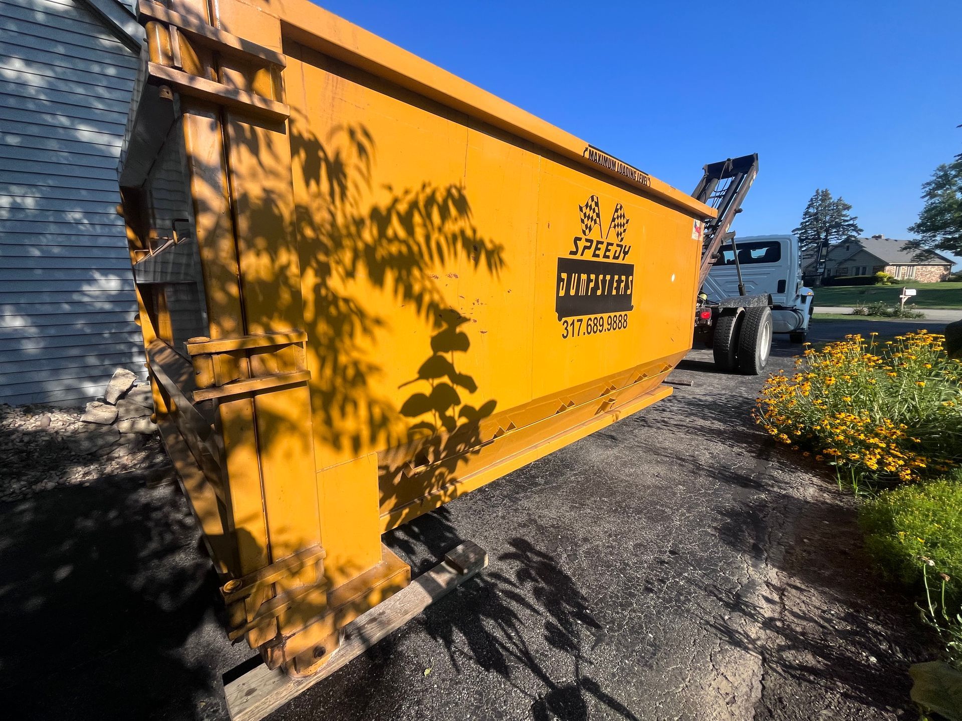 Yellow dumpster on asphalt driveway, shadows, and a truck.