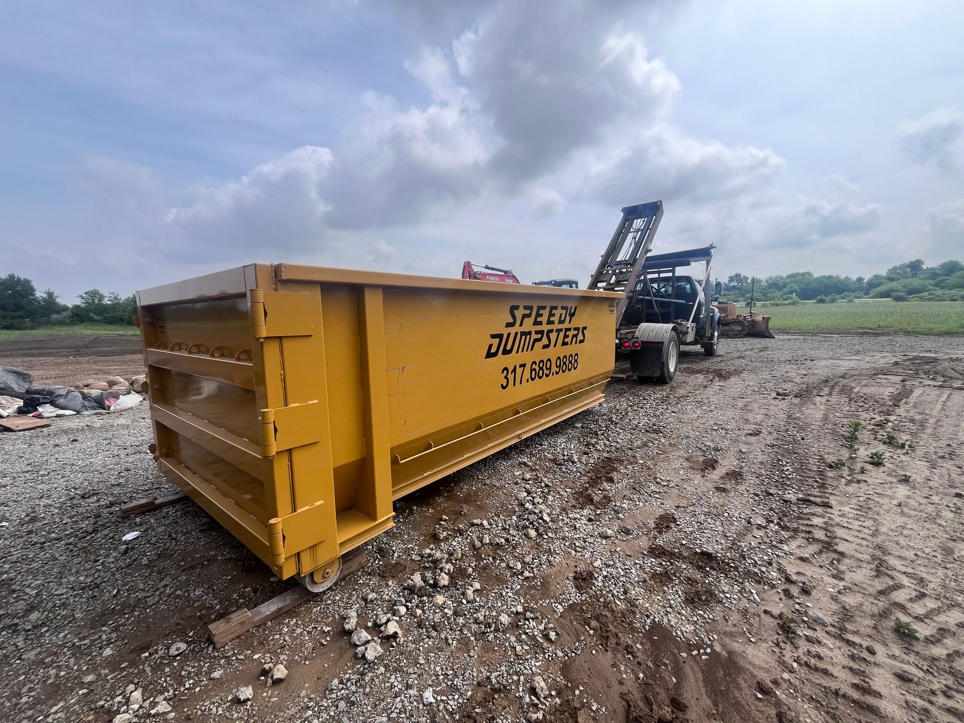 Yellow dumpster on gravel at a construction site, pulled by a truck.