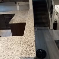 A kitchen with granite counter tops and a staircase in the background.