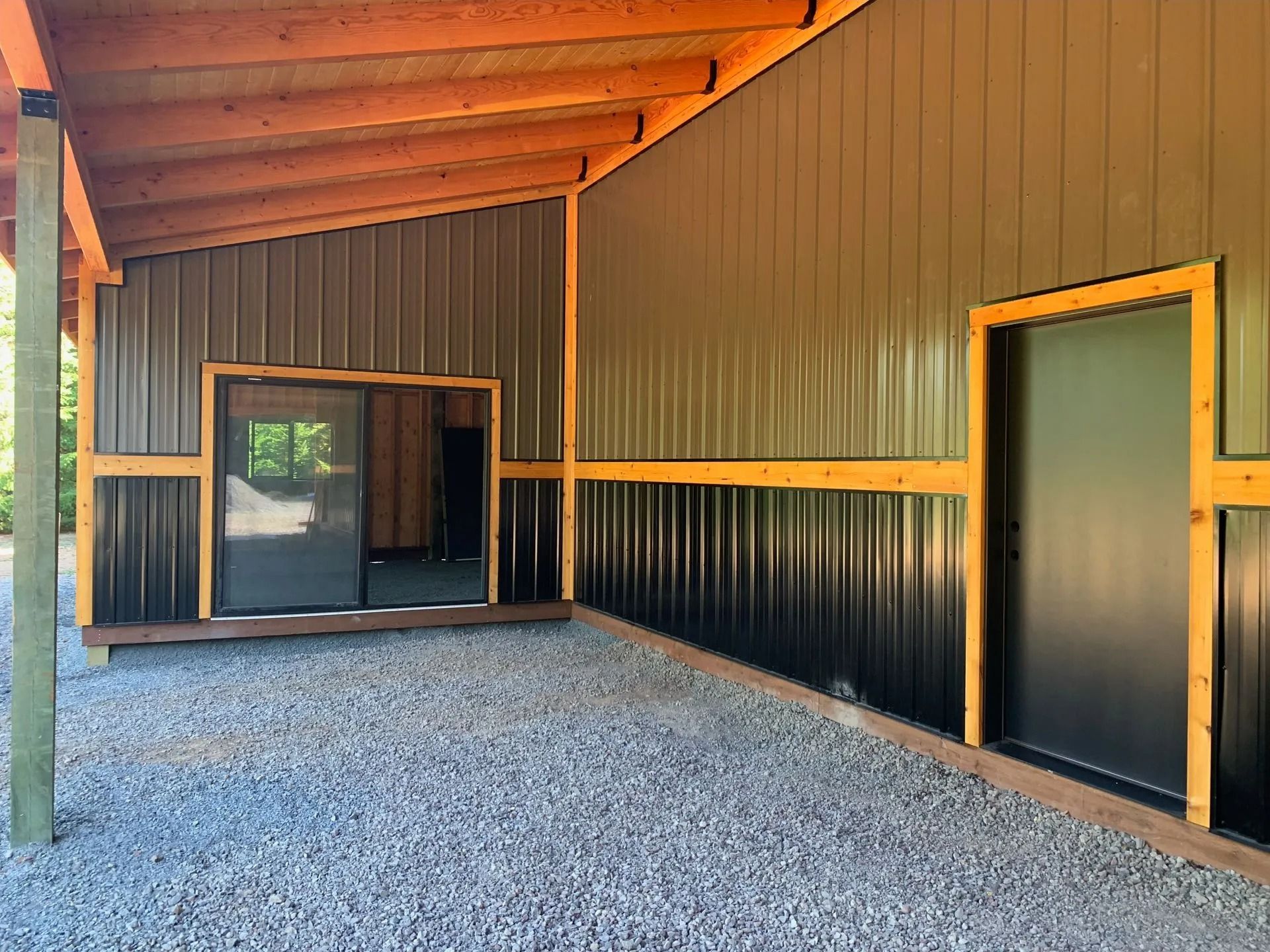 Open-air building with gravel floor, metal walls, and wooden accents. Features two dark doors and a sloped roof.