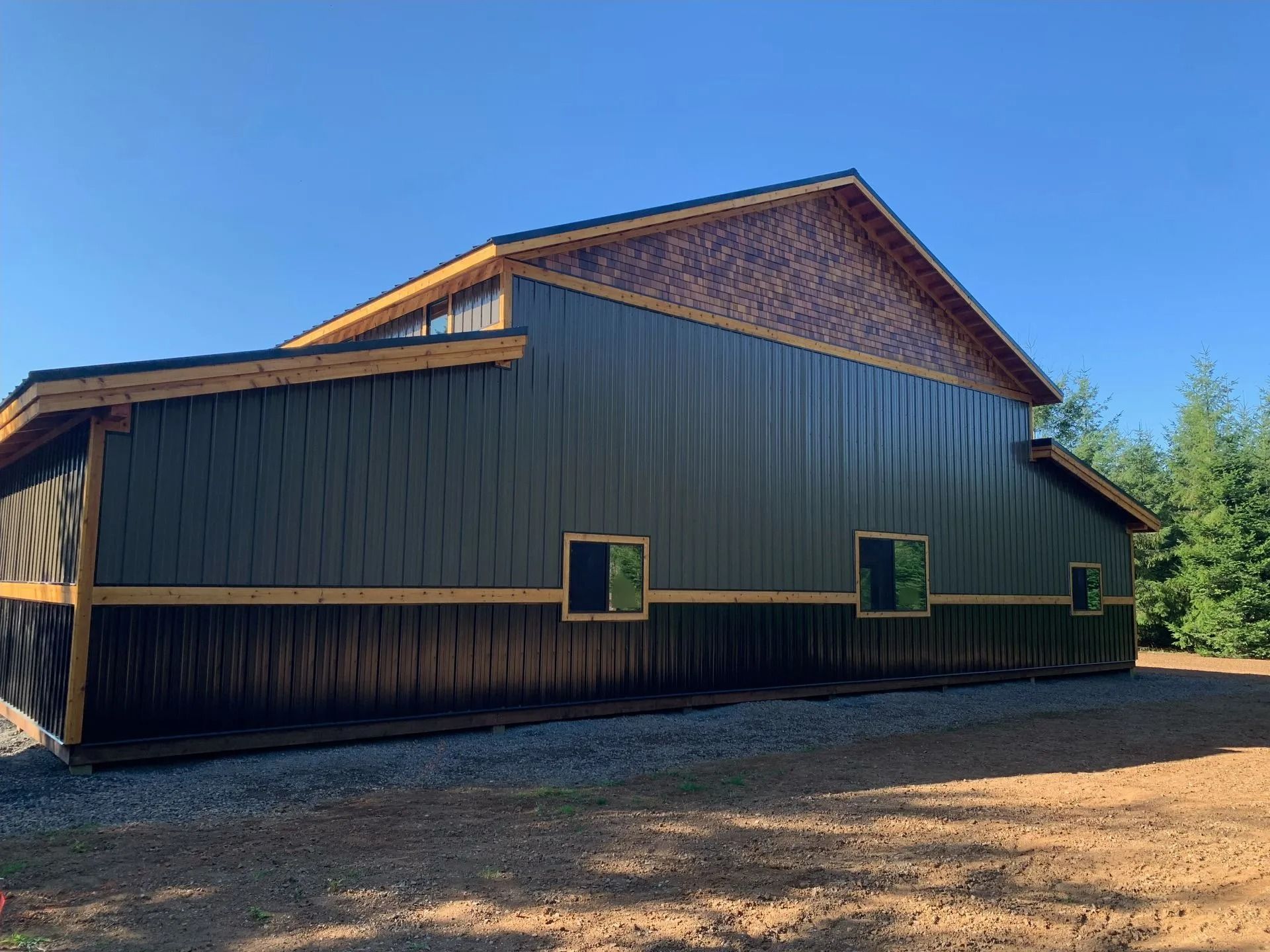 Dark green barn with brown trim and roof, set on gravel, under a blue sky.