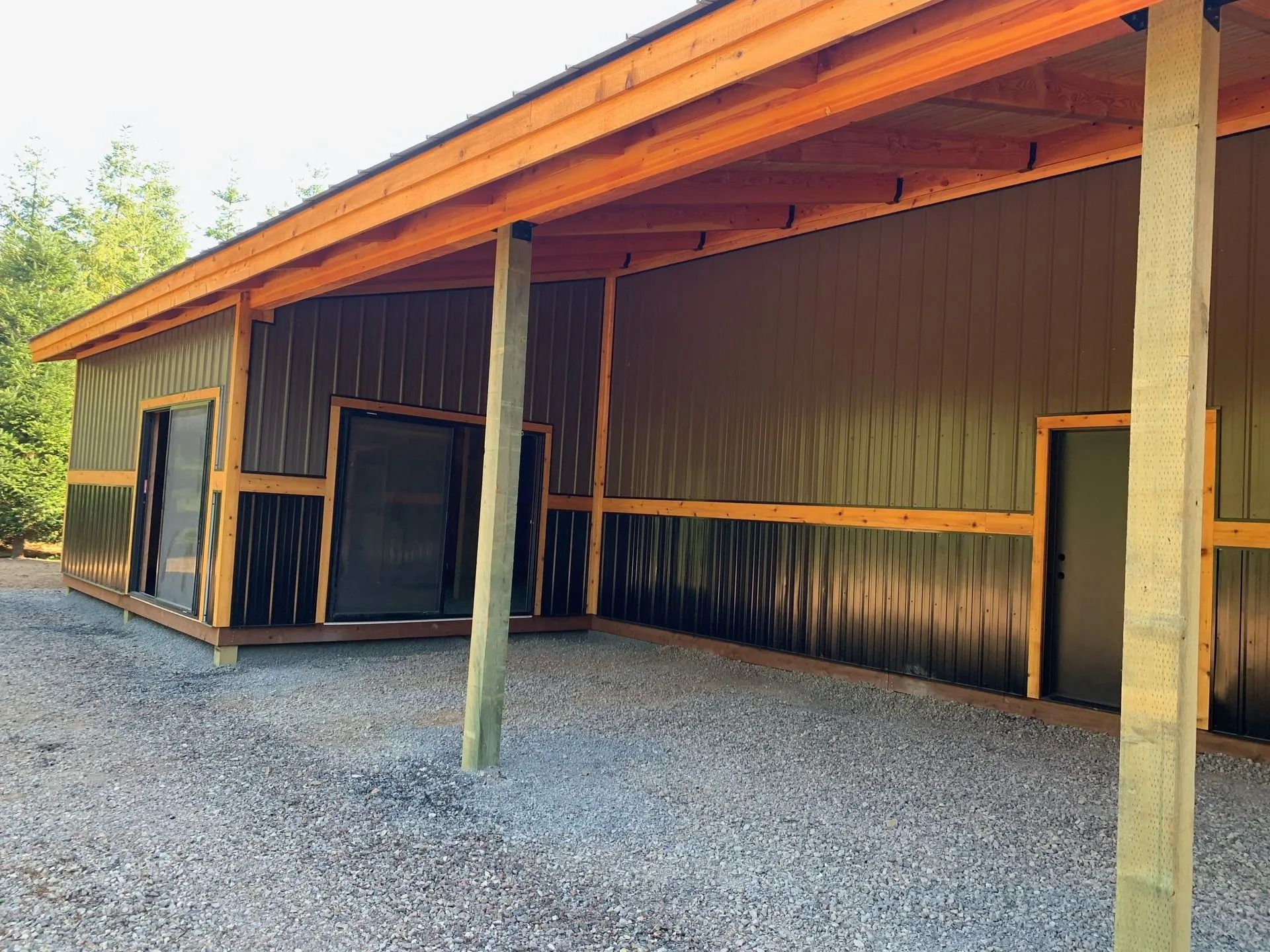 A brown and tan barn with an open-air overhang and gravel ground.