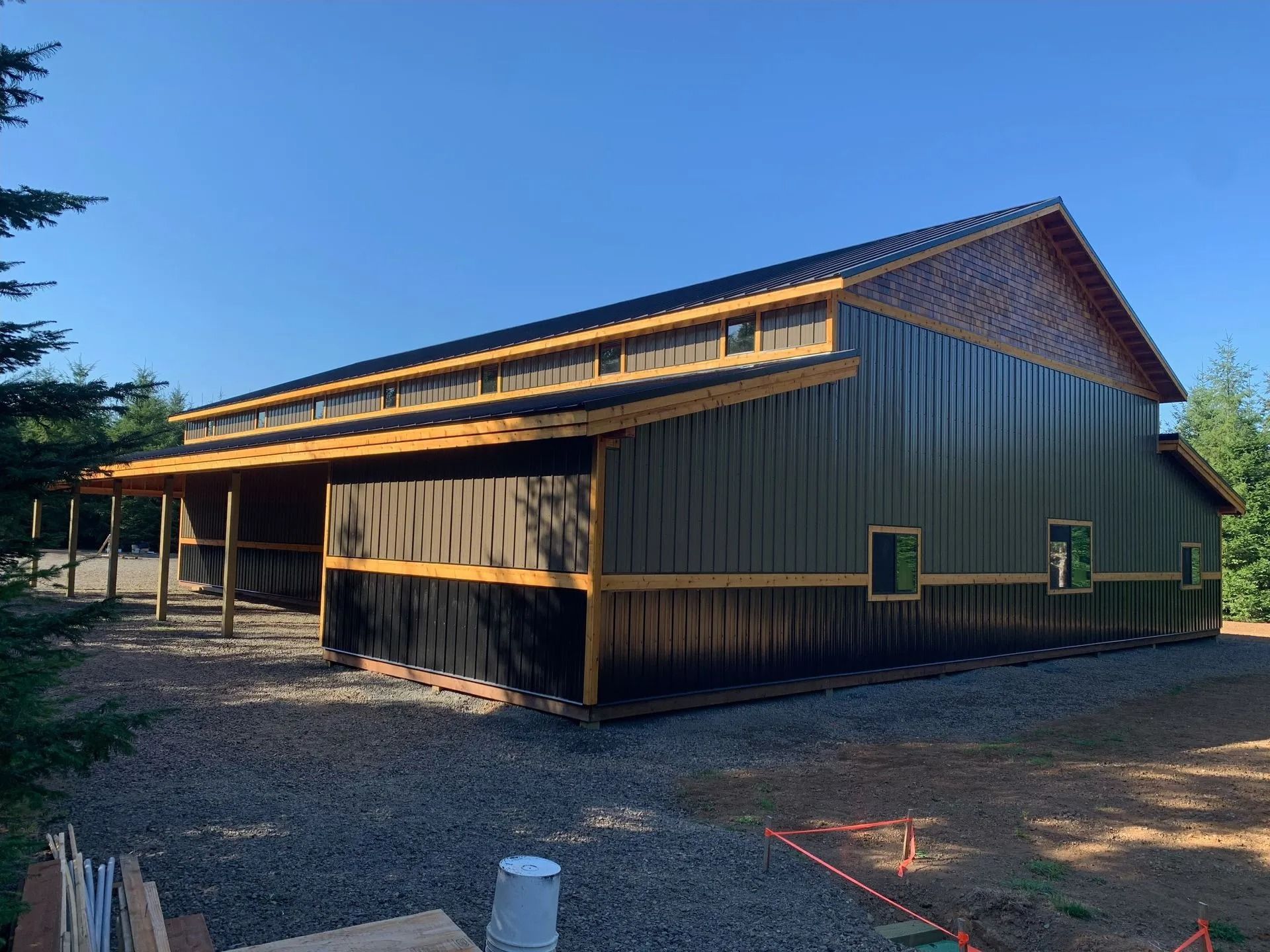 Dark green metal barn with wood trim under a clear blue sky.