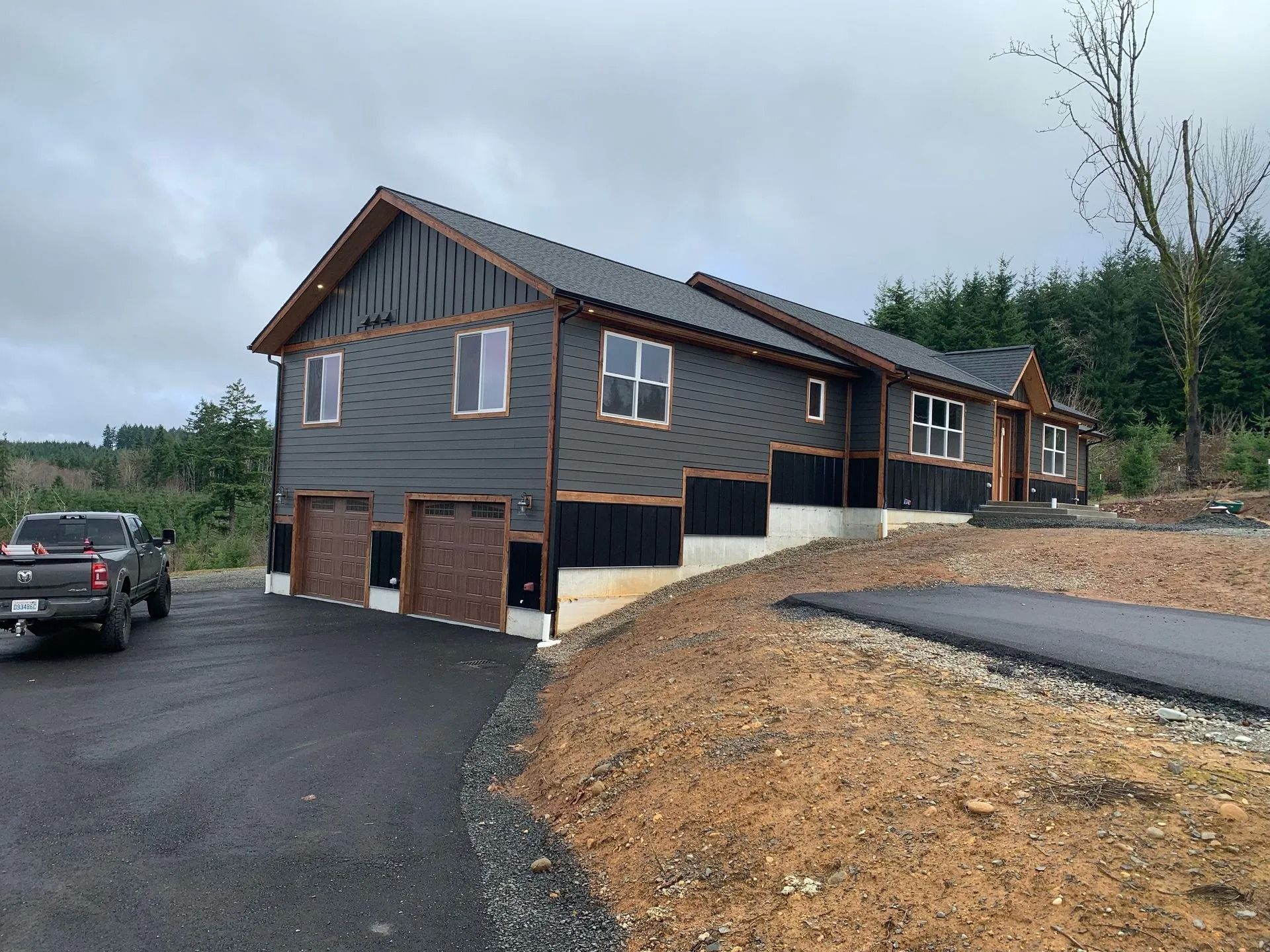 Dark gray house with brown trim and garage doors, black asphalt driveway. Truck parked on the left.