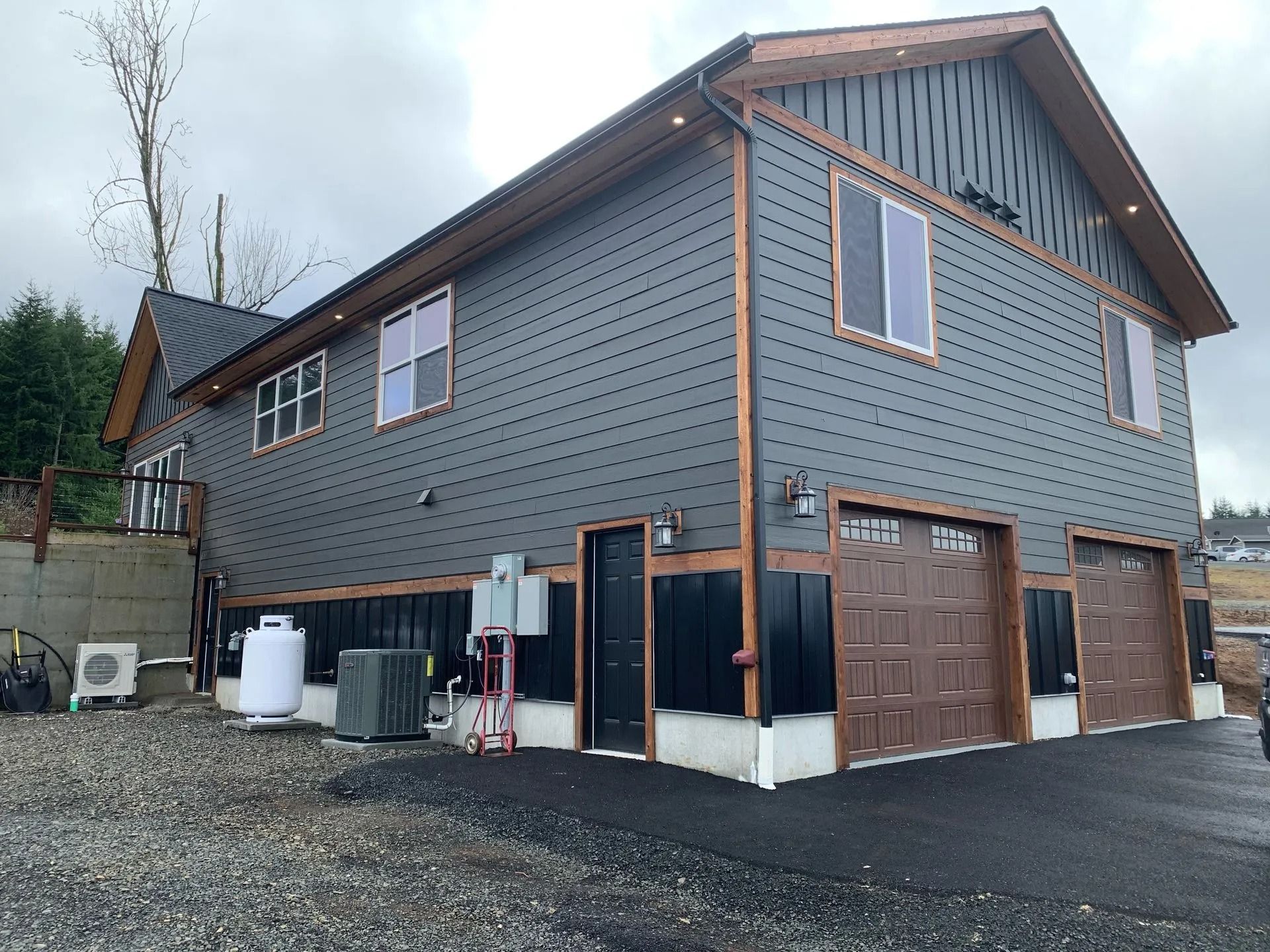 Two-story gray house with brown trim and garage doors, on a paved driveway.