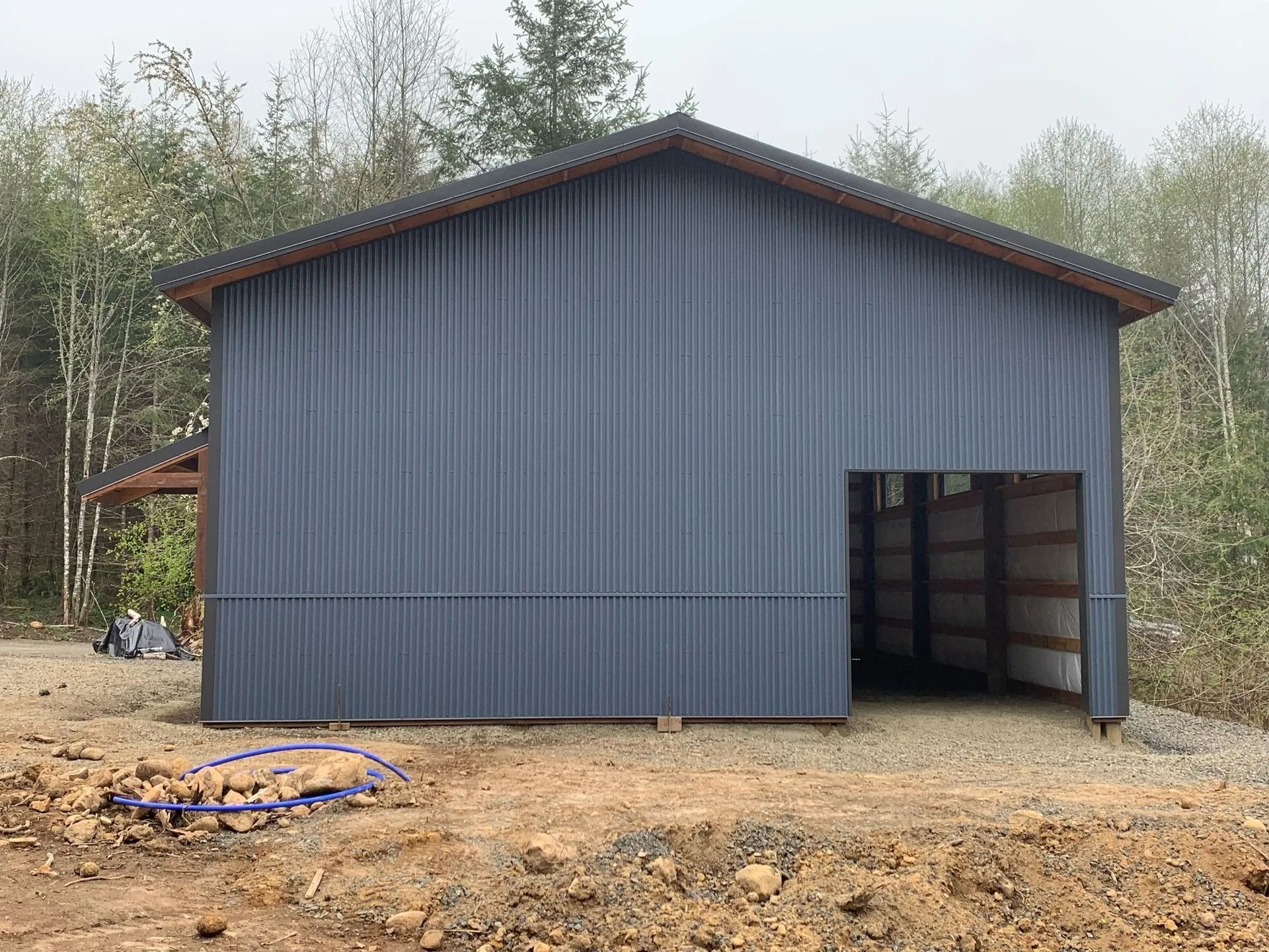 Gray metal barn with open doorway, set against a forest background.