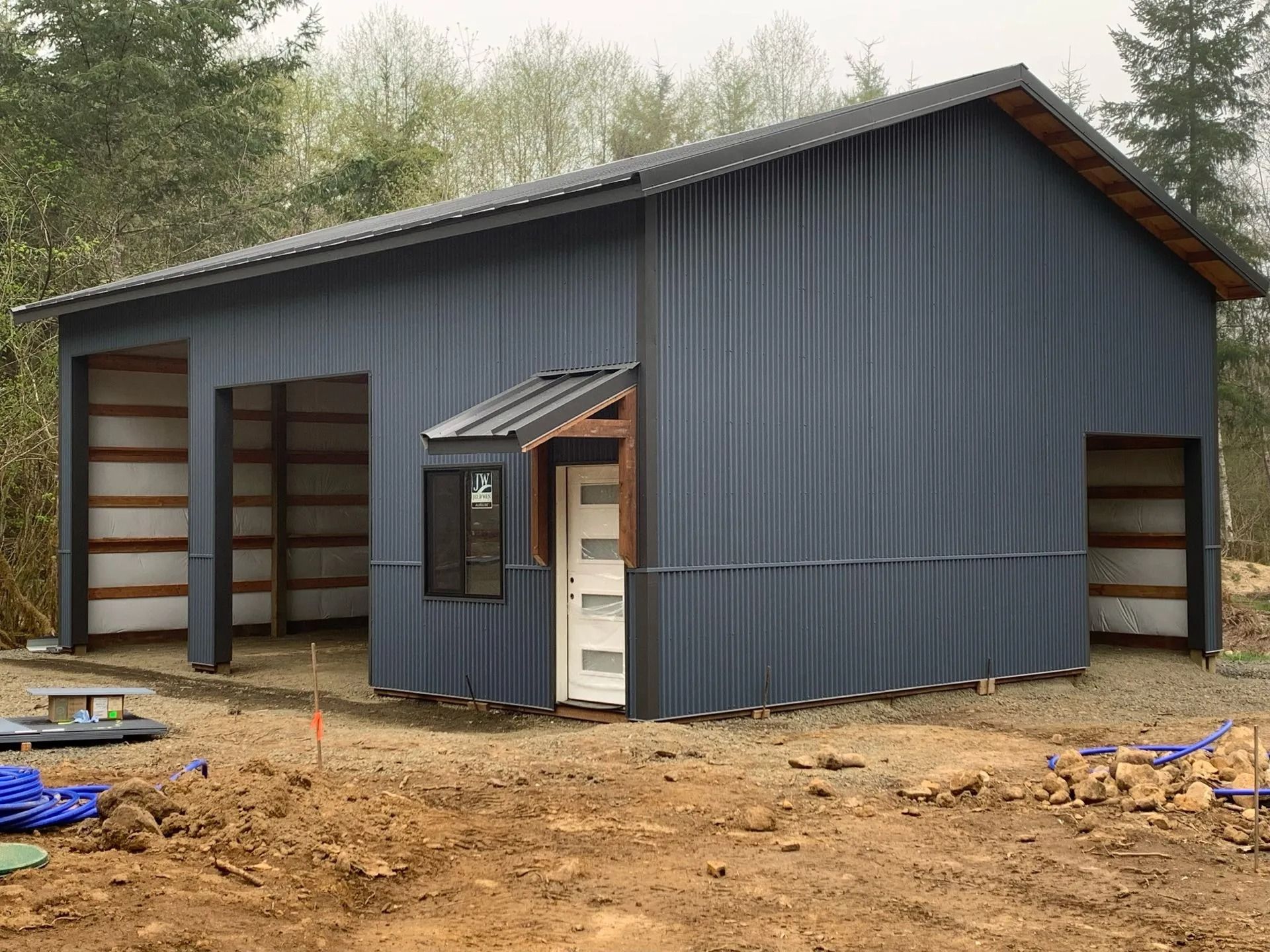 Blue metal-sided outbuilding with garage bays and an entrance, in a natural setting.