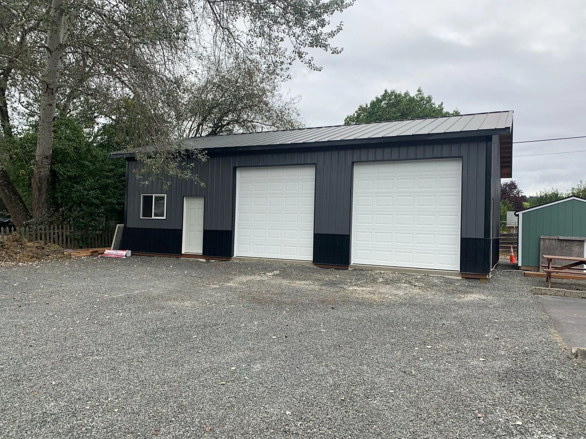 Gray metal garage with white garage doors and a gravel driveway.