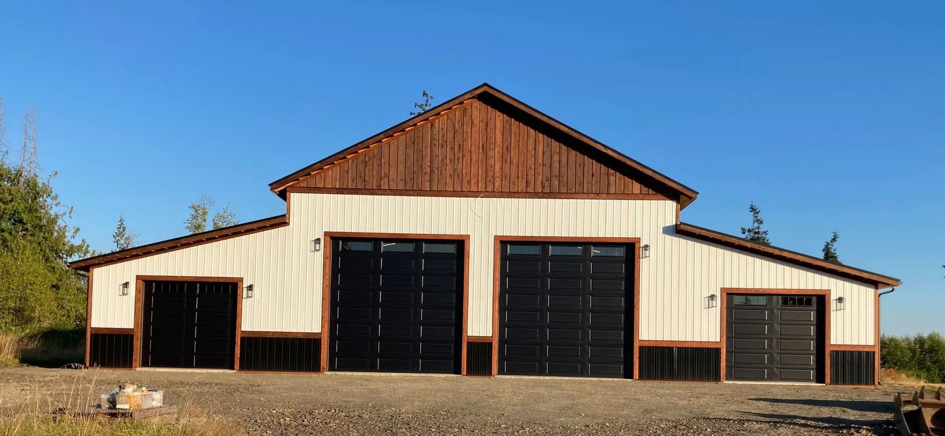 A white barn with brown trim, black garage doors, and a blue sky.