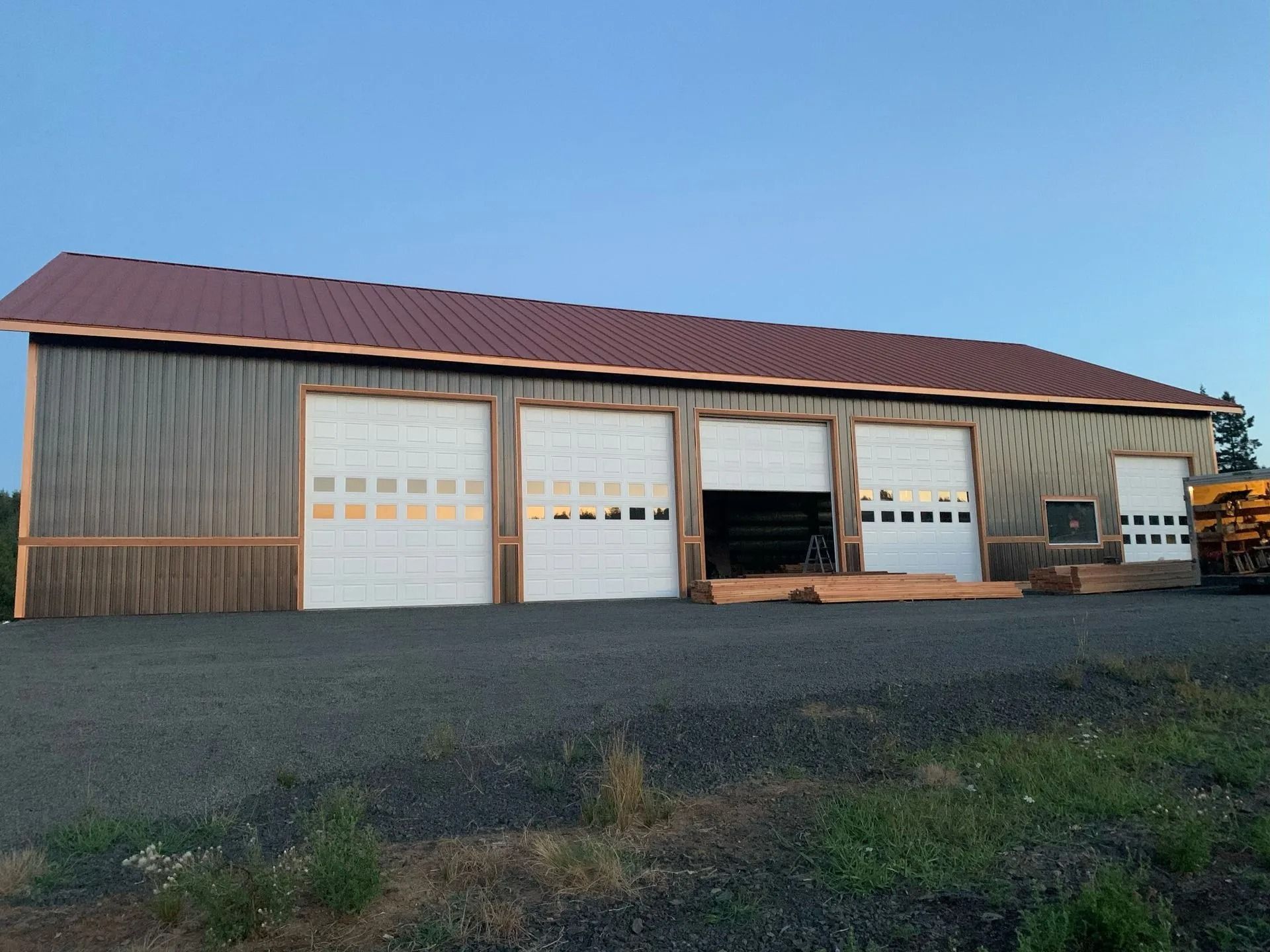 Gray metal building with four garage doors; red roof, gravel driveway.