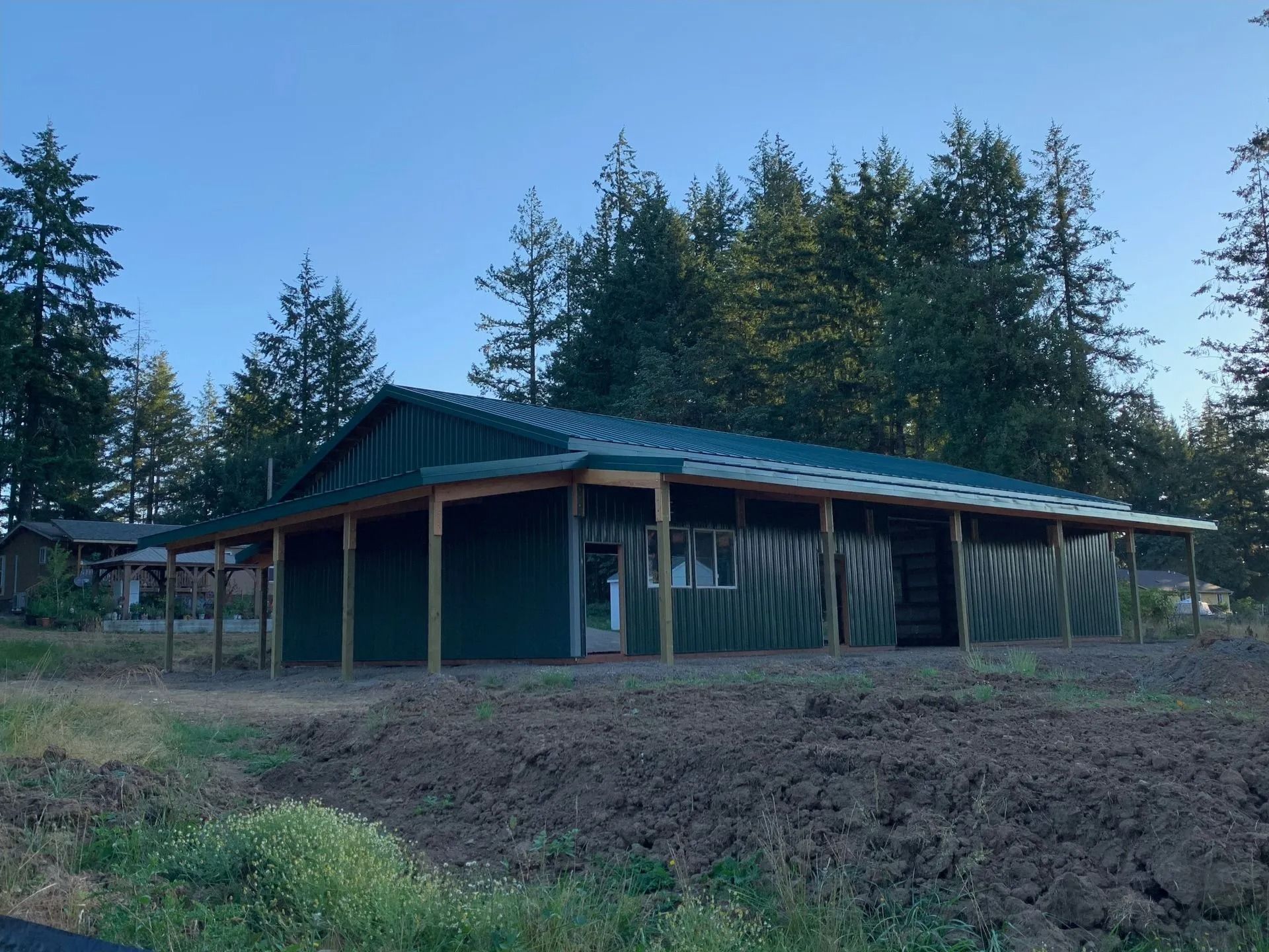 Green building with porch, forest backdrop, and a dirt patch in the foreground.