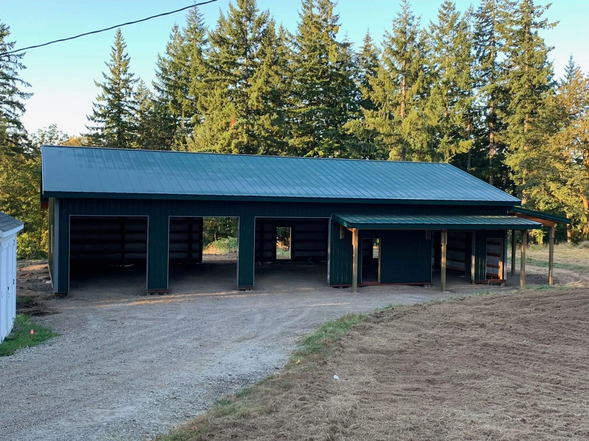 Green metal roof carport with three bays and a covered side area on gravel driveway.