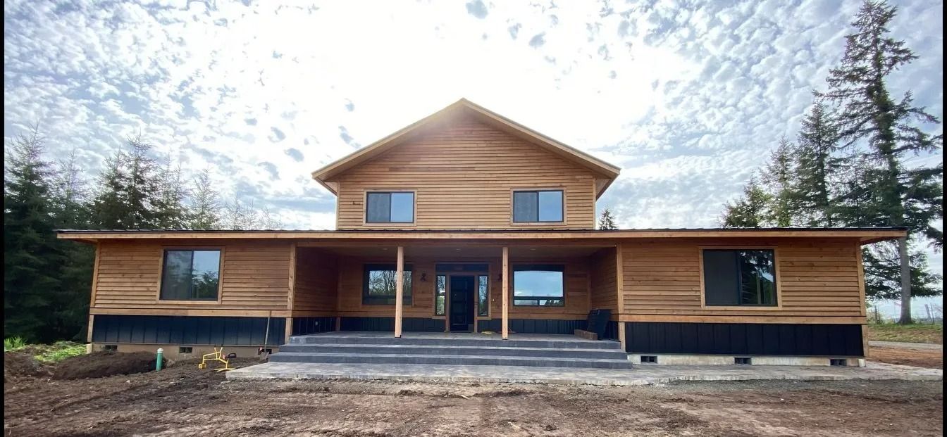 Wood-sided house under cloudy sky.  Long porch with pillars.  Large windows.  Dirt and trees around house.