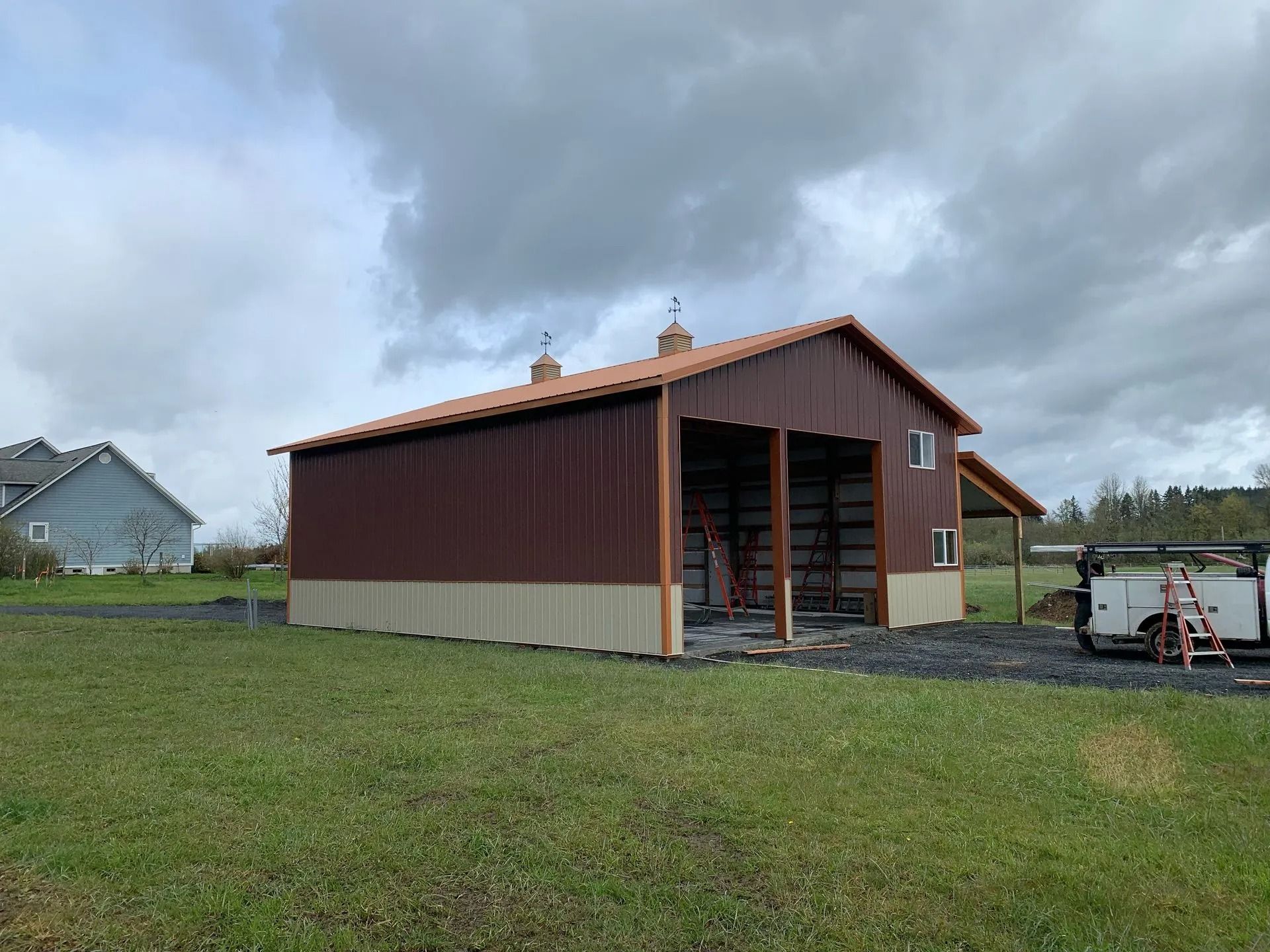 Brown and tan metal barn under a cloudy sky in a grassy field.