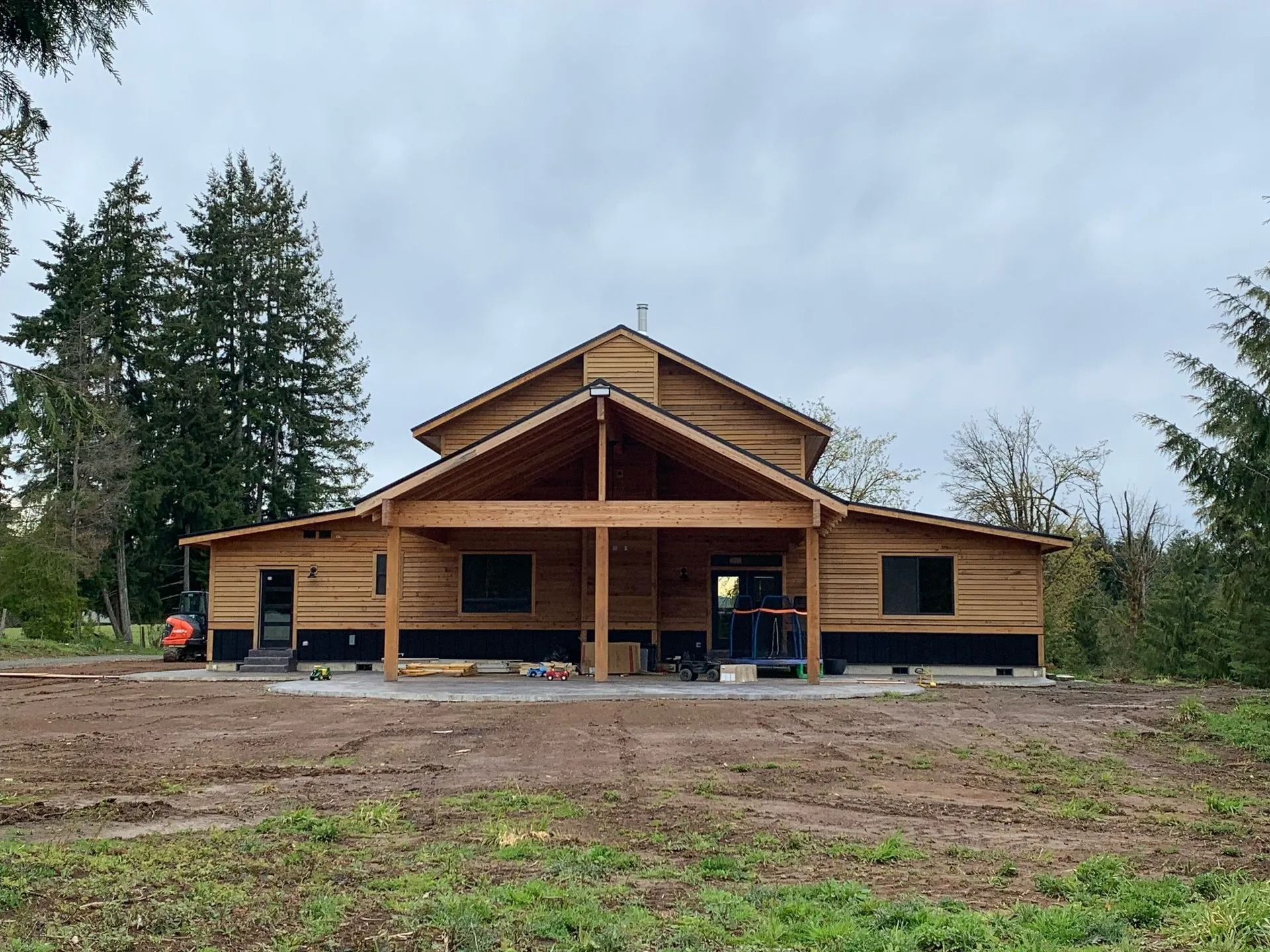 Building in progress; unfinished wooden structure with covered porch and large windows on a cloudy day.