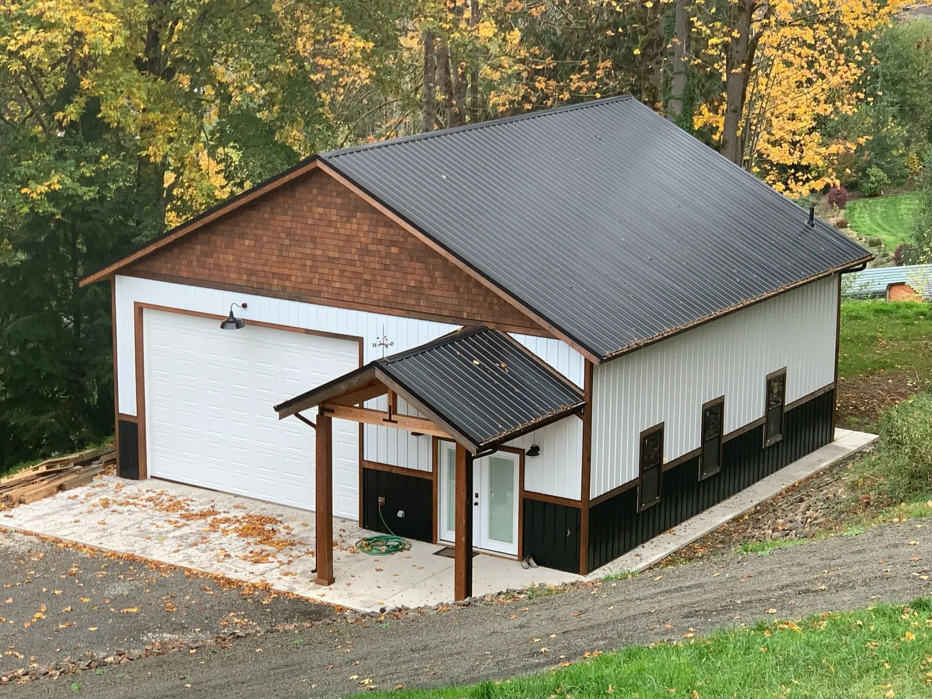 White and black metal building with black roof, garage door, and small covered entrance.