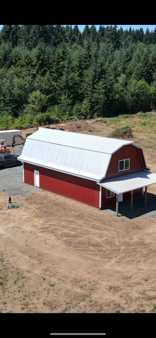 Red barn with a white roof in a field with a forest in the background.
