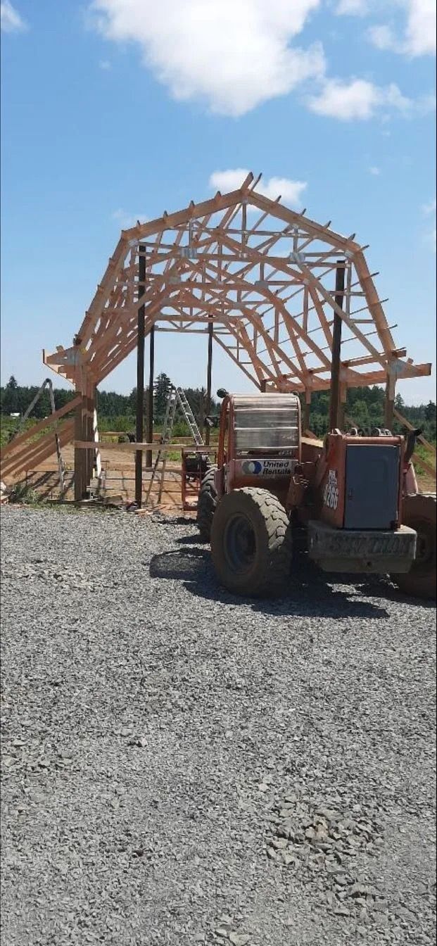 A wooden roof under construction with an orange tractor on a gravel surface under a blue sky.