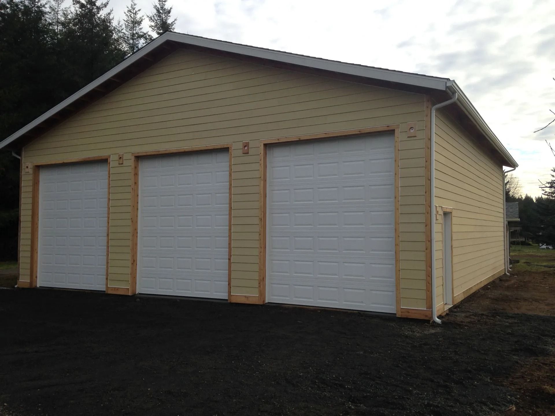 Yellow three-bay garage with white doors, light-colored trim, and a dark asphalt driveway.