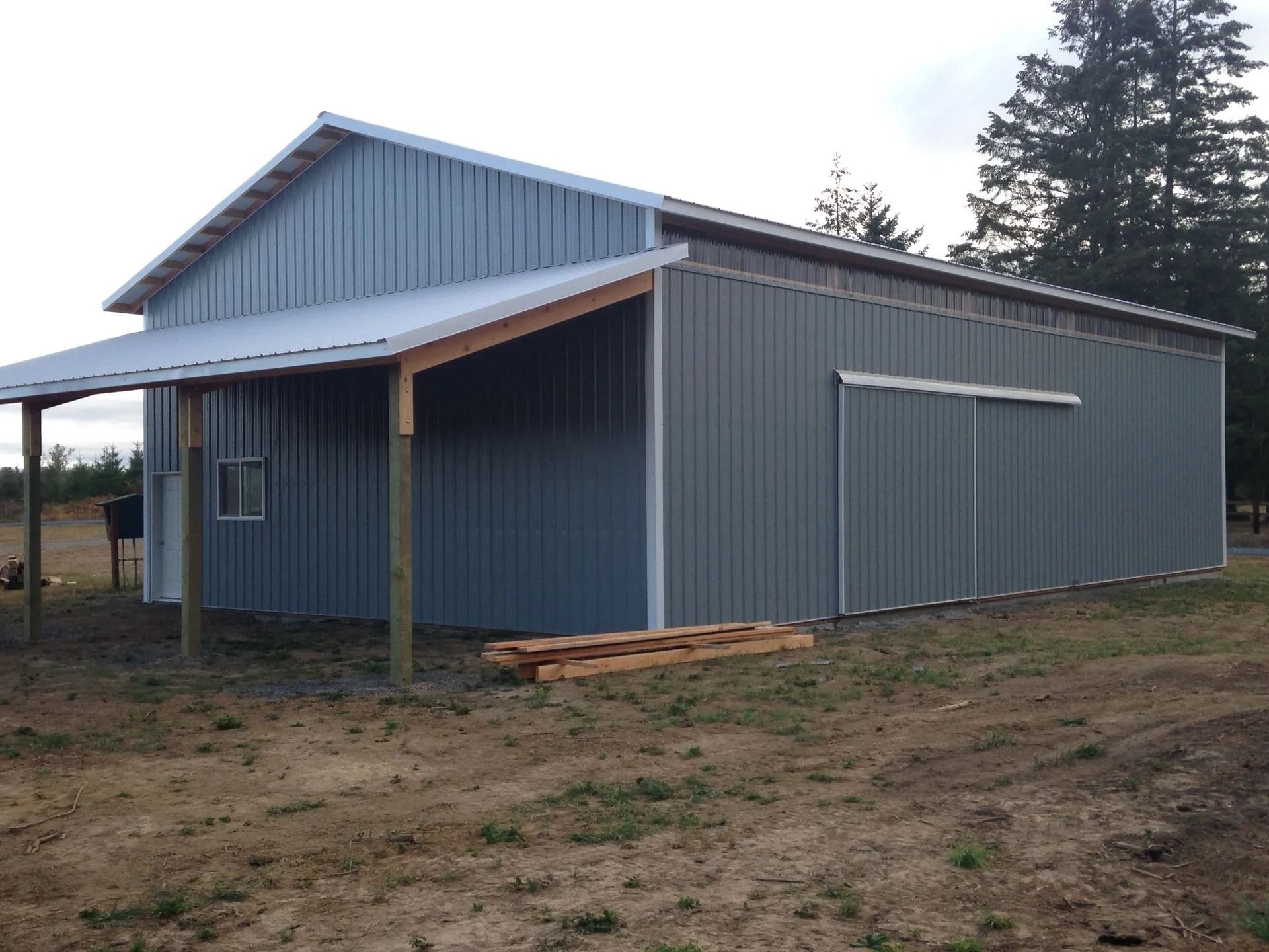 Gray metal barn with a covered porch and sliding door, set in a field.