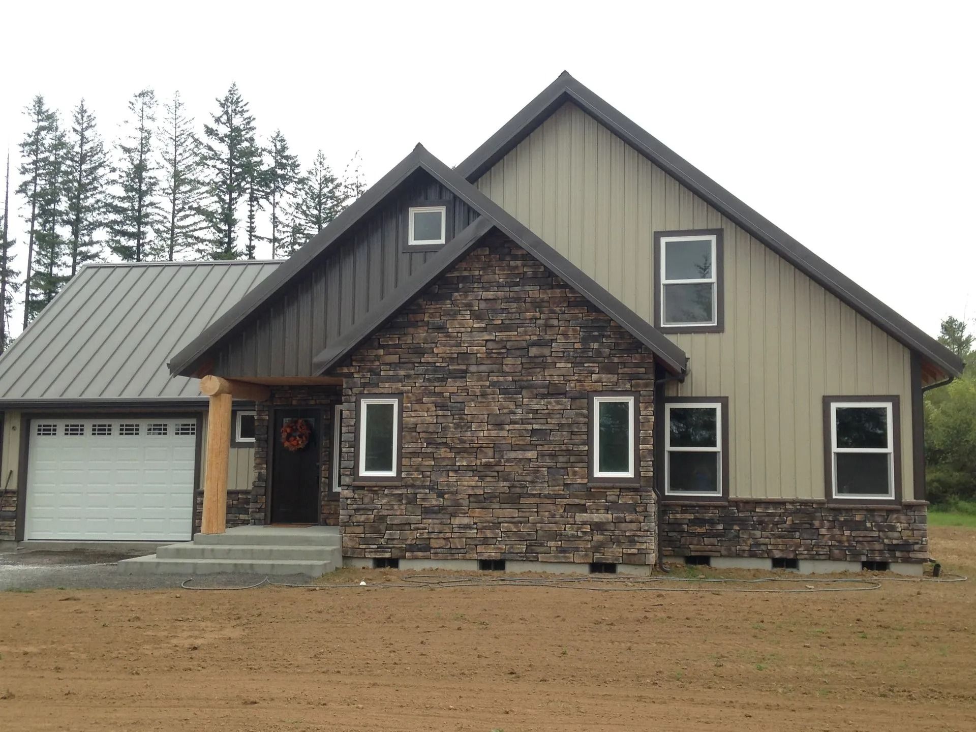 Modern house with brown stone and tan siding, a metal roof, and a garage door.