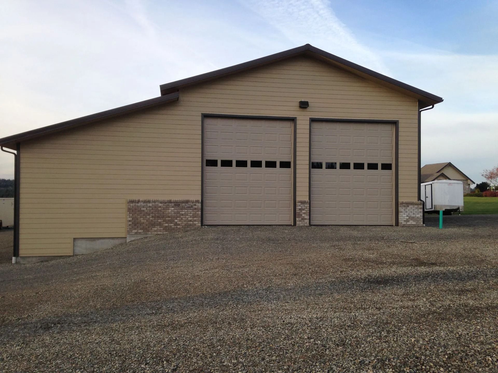Tan two-bay garage with matching garage doors, gravel driveway, and a small brick section.