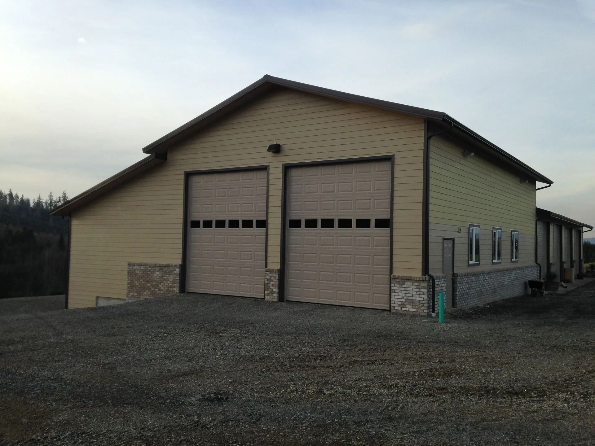 Tan garage building with two garage doors and gravel driveway.