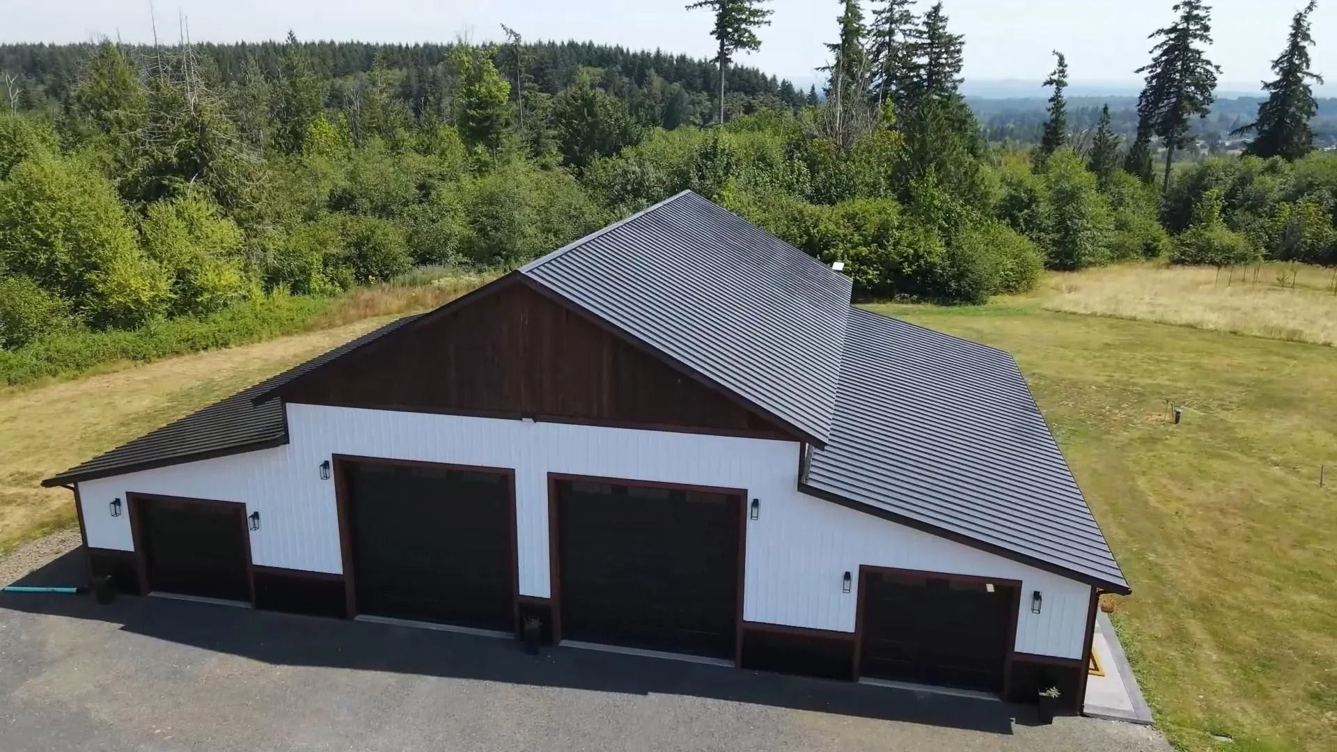 White and brown barn-style building with three garage doors, set against a green forest background.
