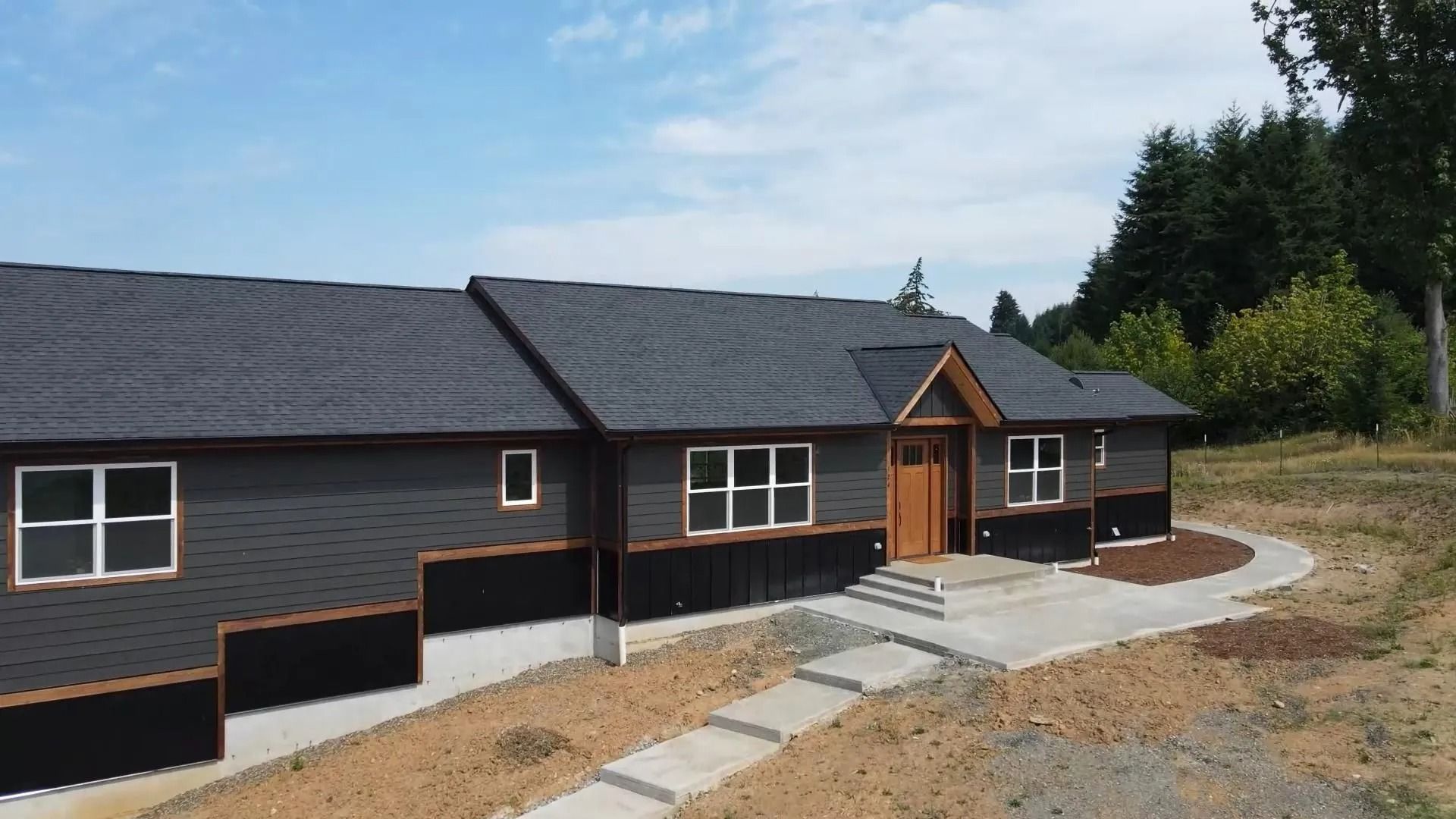 Gray house with dark roof and brown trim, pathway leading to the front door.