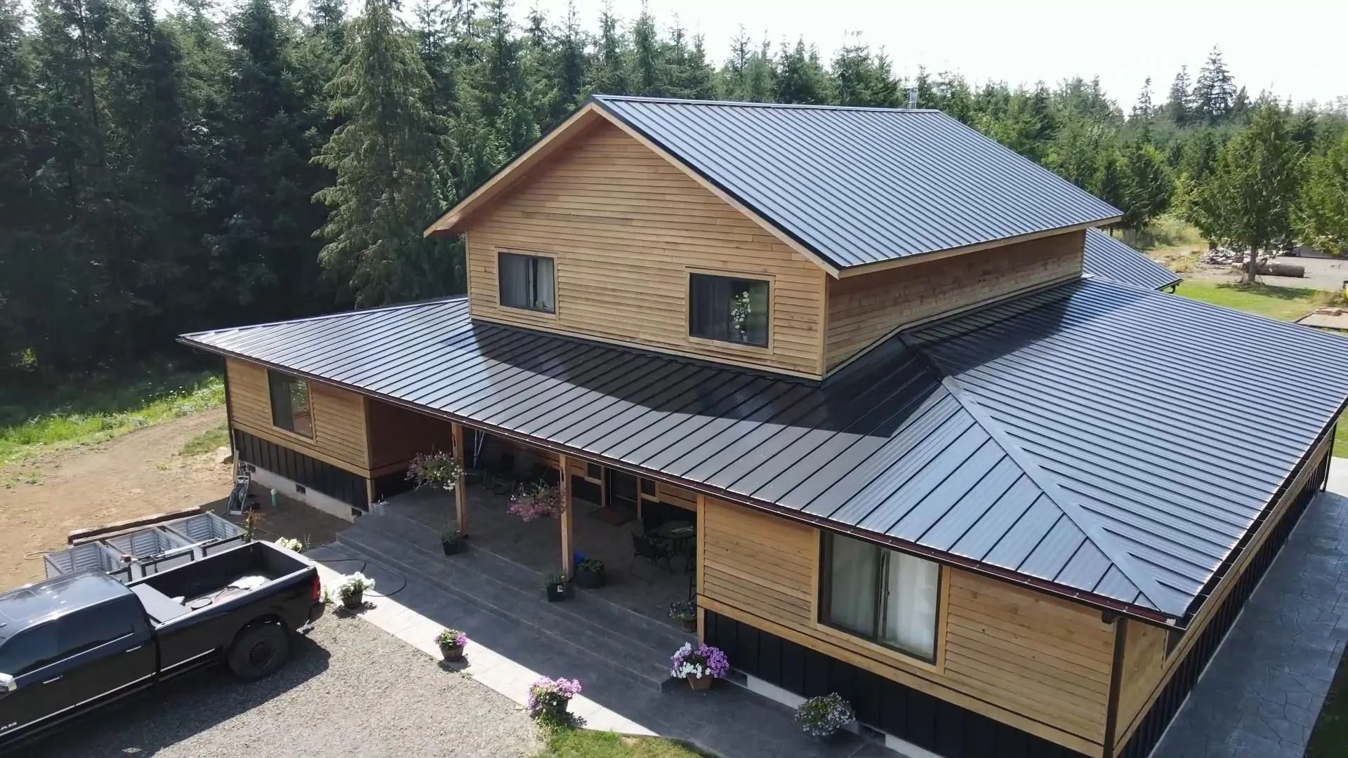 House with a black metal roof and wood siding, sitting on a concrete slab in a wooded area.