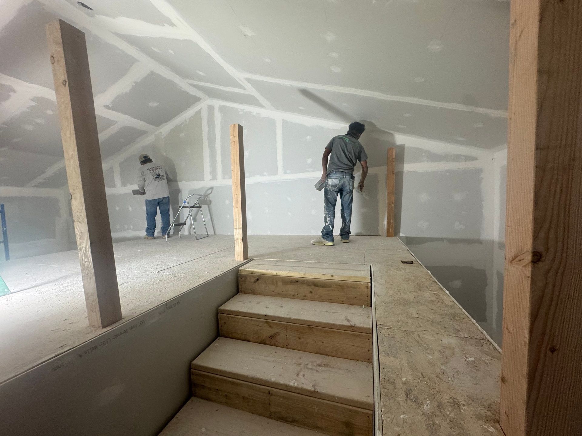 A man is standing on a wooden platform in a room under construction.