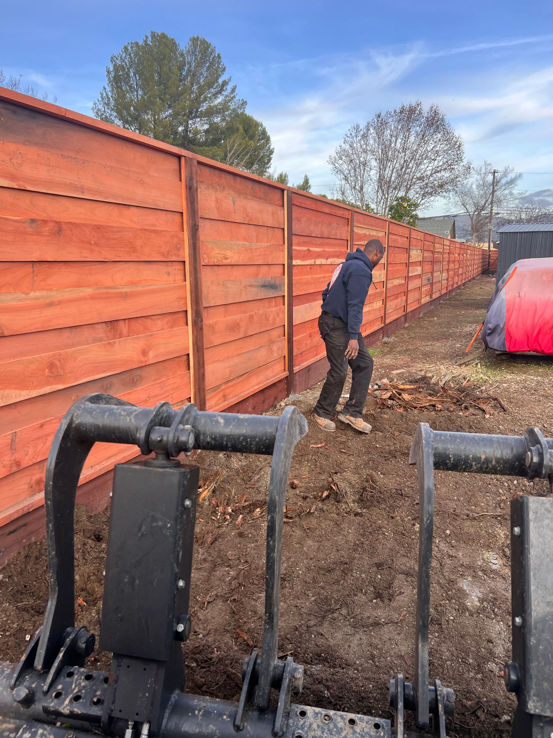 A man is standing in the dirt in front of a wooden fence.