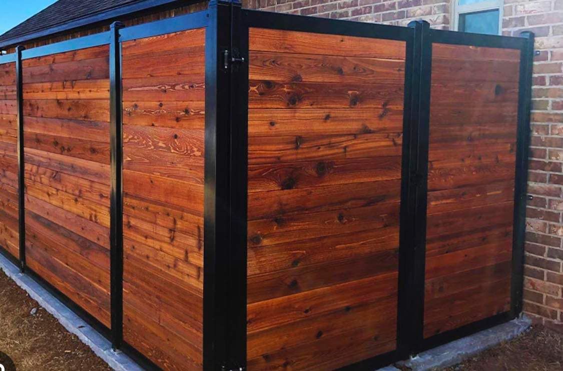 A wooden fence with a black frame is sitting next to a brick building.