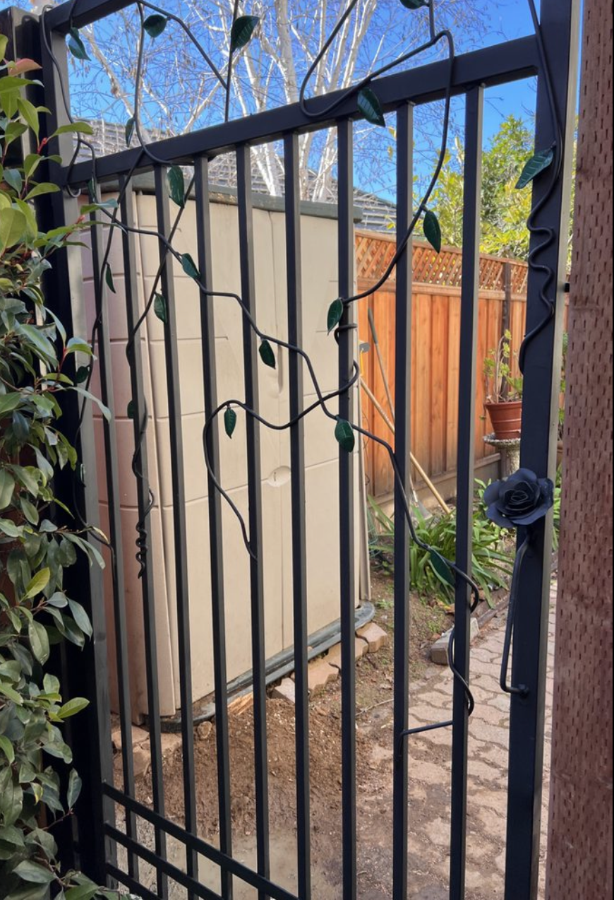 A wrought iron gate with leaves on it is leading to a shed.