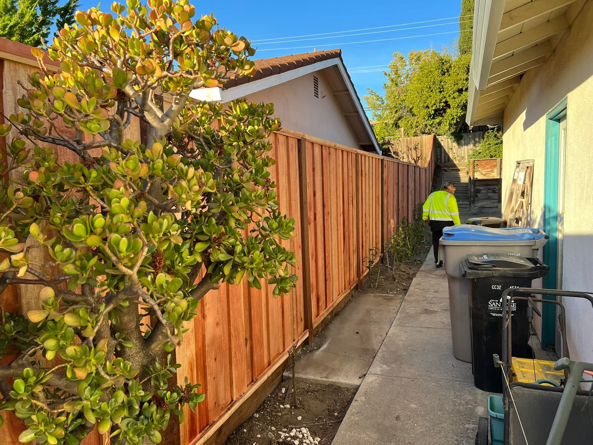A man is walking down a sidewalk next to a wooden fence.