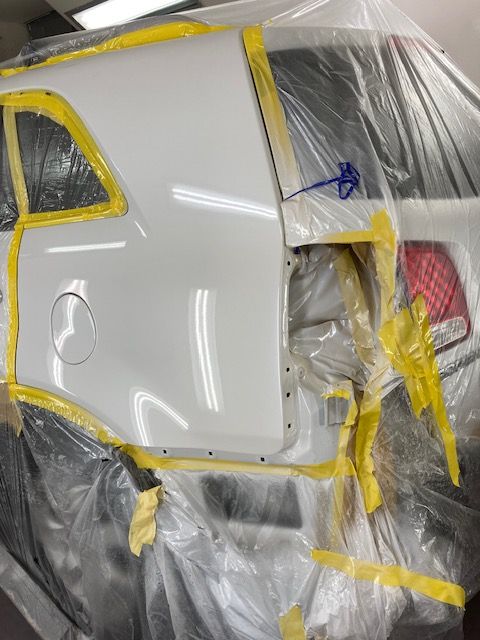 White car panel, taped and plastic-covered, ready for paint in a workshop.