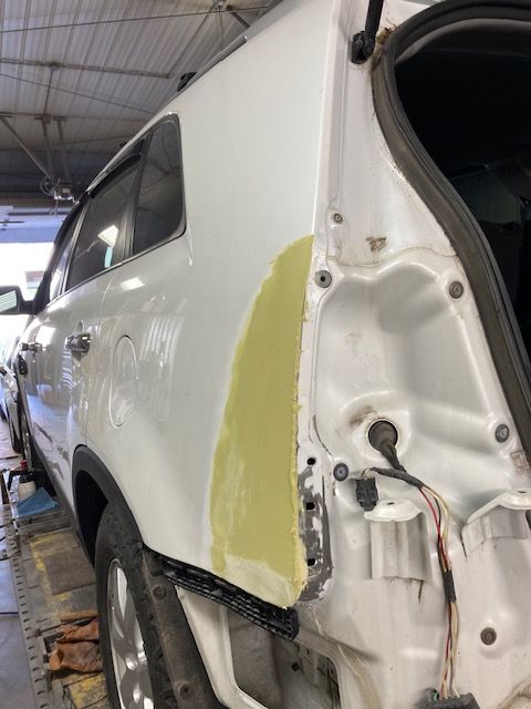White SUV rear quarter panel with body filler, in a repair shop.