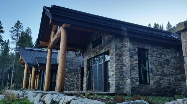 Modern stone lodge with tall wooden columns and large windows in a wooded mountain setting