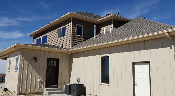 Tan house exterior with gray roof, beige siding, and blue sky on a sunny day