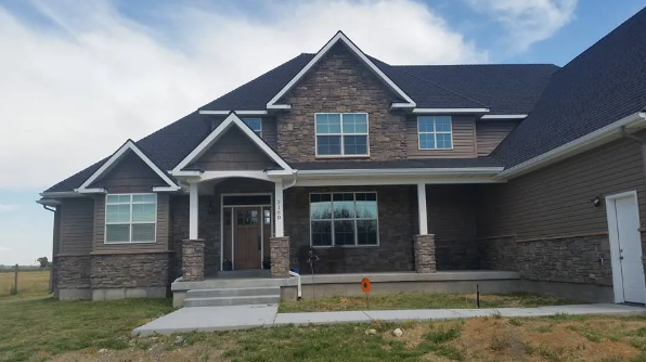 New suburban house with stone and siding exterior, front porch, and unfinished lawn under a cloudy sky