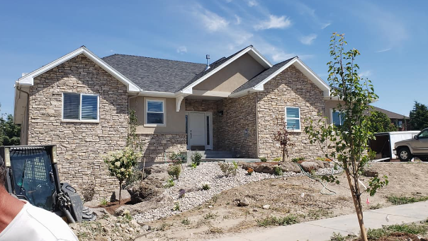 Stone house with a front porch and desert landscaping under a clear blue sky.
