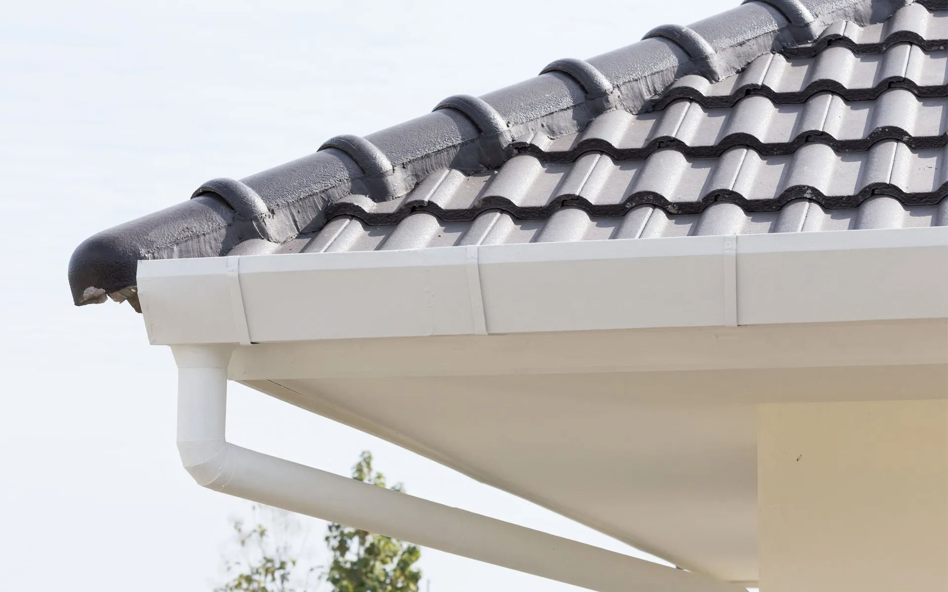 White gutter and downspout under a gray tiled roof on a house eave