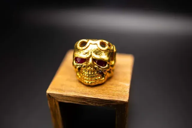A gold ring with a skull on it is sitting on top of a wooden box.