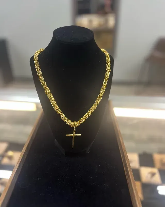 A gold necklace with a cross pendant on a mannequin