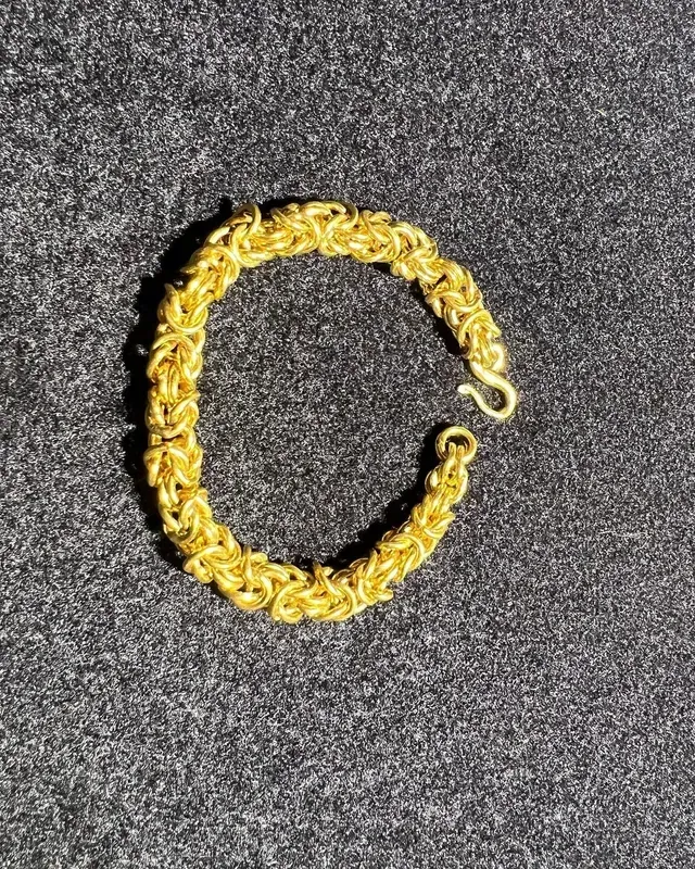 A close up of a gold chain bracelet on a gray surface.
