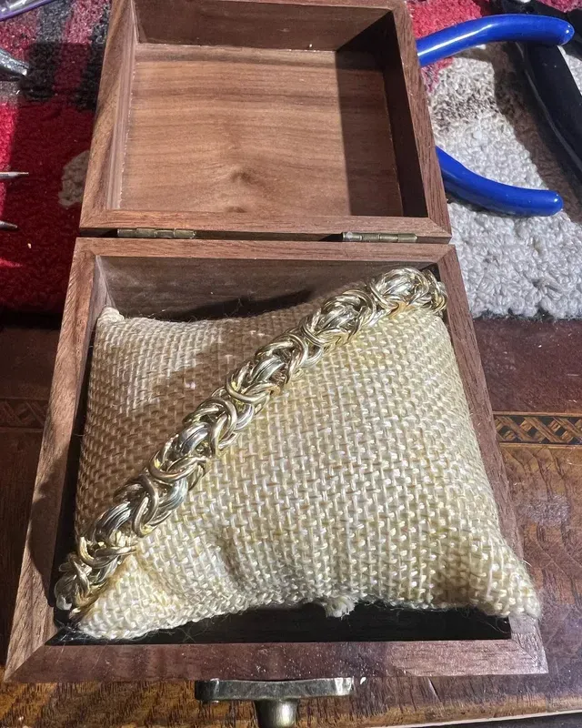 A bracelet is sitting on a pillow in a wooden box.